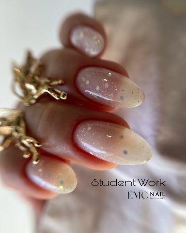 Ongles en dégradé nude avec paillettes, main ornée d'un bijou doré.