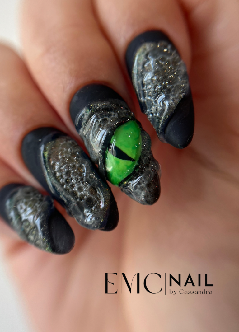 Ongles longs noirs avec motifs texturés, un accent vert en forme d'œil.