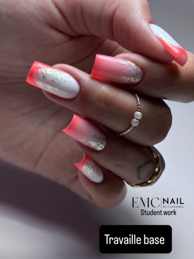 Main avec des ongles longs rose et blancs, ornés de paillettes et une bague dorée.